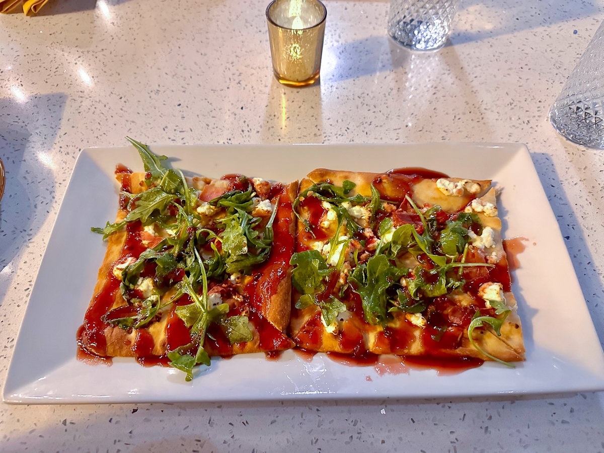 flatbread with crumbled cheese and a redish pink sauce with arugula